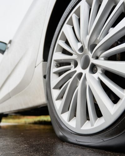 Stopped white car with punctured car tire on a roadside Close up view on stopped white car with punctured car tire on a road. Focus on a wheel.